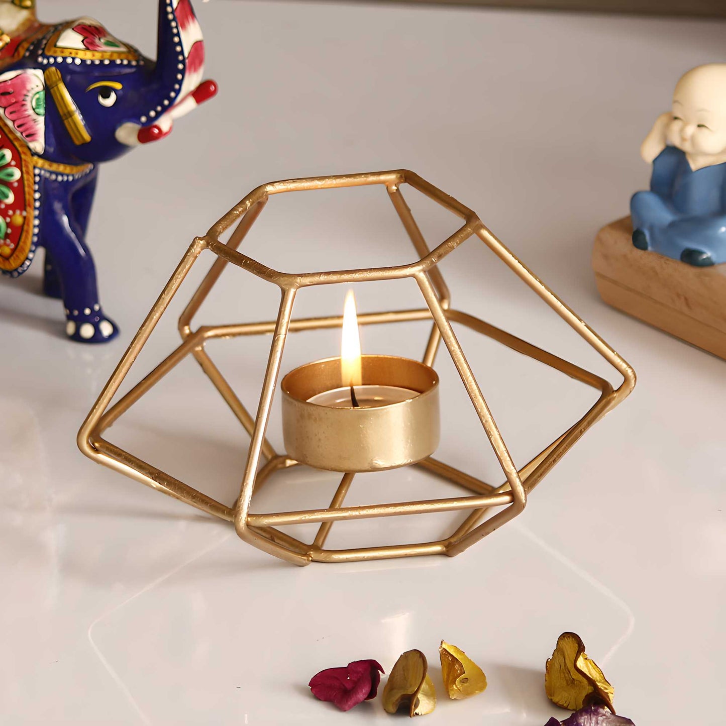 Gold geometric candle holder with a lit tealight candle on a white surface with decorative elements.