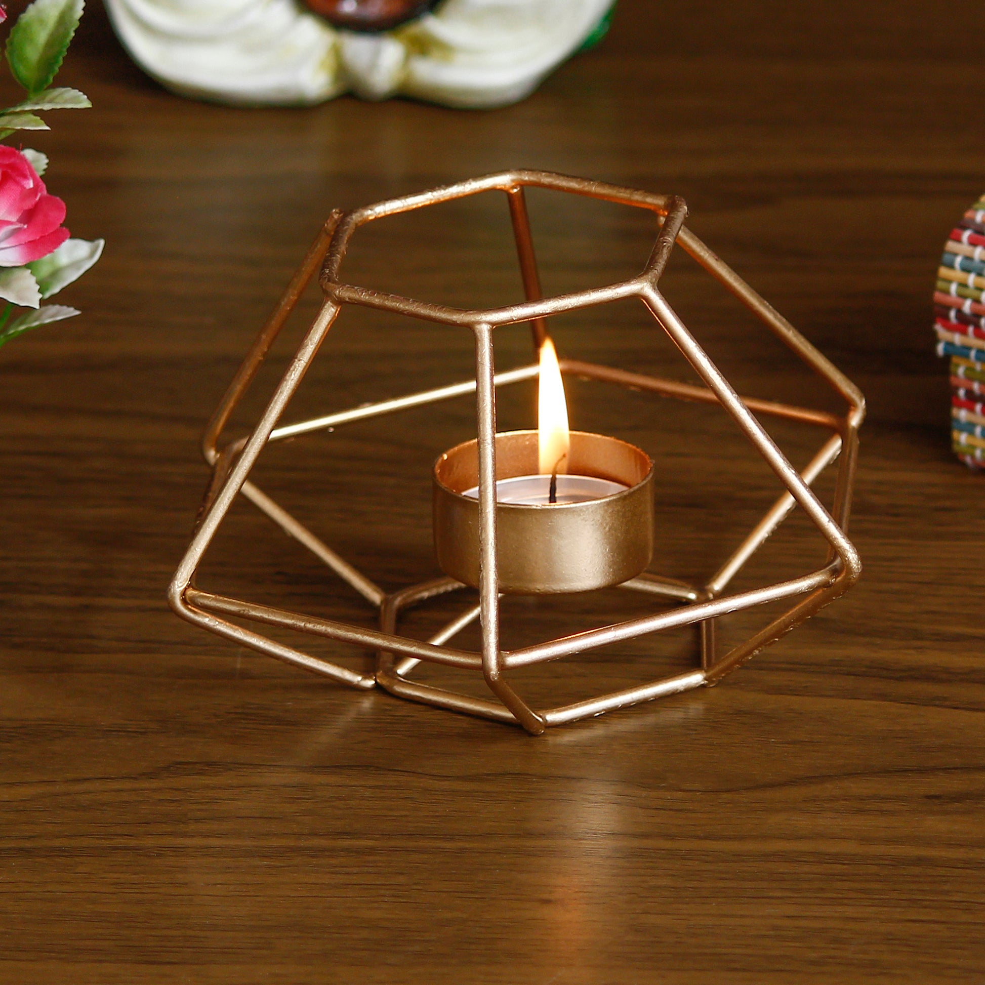 Geometric gold candle holder with a lit candle on a wooden surface